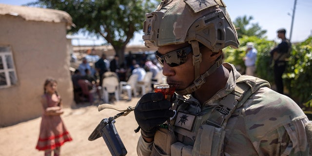 U.S. Army soldier sips tea passed out by local residents as his commanding officer and allied troops meet with local villagers on May 26, 2021, near the Turkish border in northeastern Syria. 