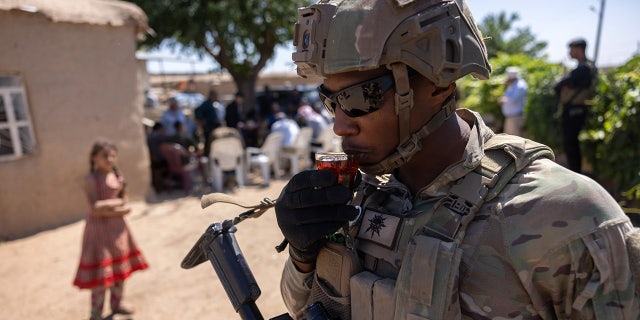 U.S. Army soldier sips tea passed out by local residents as his commanding officer and allied troops meet with local villagers on May 26, 2021, near the Turkish border in northeastern Syria. 