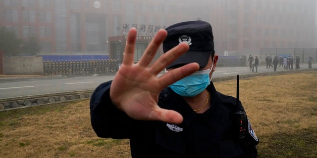 A guard leads journalists away from the Wuhan Institute of Virology.