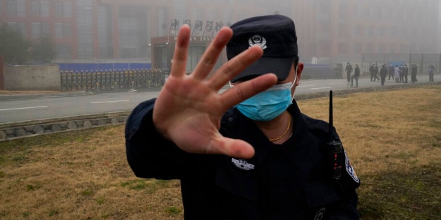 A security person moves journalists away from the Wuhan Institute of Virology