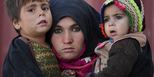 An Afghan woman holds her children as she waits for a consultation outside a makeshift clinic at a sprawling settlement of mud brick huts housing those displaced by war and drought near Herat, Afghanistan, Dec. 16, 2021.