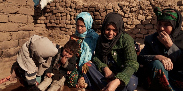 Aziz Gul, second from right, and her 10-year-old daughter Qandi, center, sit outside their home with other family members, near Herat, Afghanistan, Dec. 16, 2021. Qandi's father sold her into marriage without telling his wife, Aziz, taking a down-payment so he could feed his family of five children. Without that money, he told her, they would all starve. He had to sacrifice one to save the rest.
