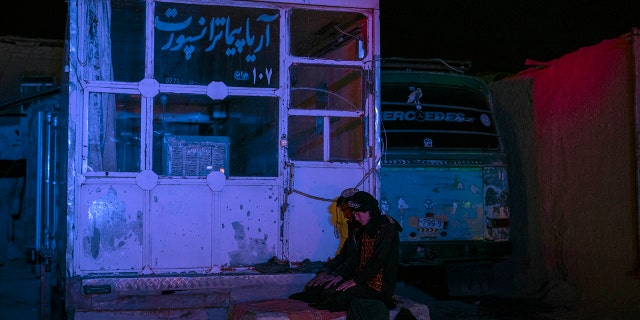 Two Afghan men pray at a bus station in Herat, Afghanistan, on Tuesday, Nov. 23, 2021, before they embark on a bus for a 300-mile trip south to Nimrooz near the Iranian border.