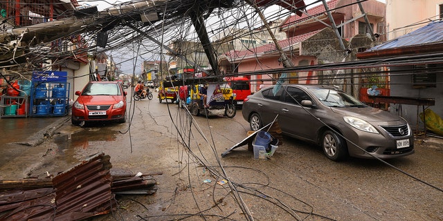 Sur cette photo fournie par Greenpeace, des voitures passent devant un poteau électrique renversé en raison du typhon Rai dans la ville de Surigao, Surigao del Norte, dans le sud des Philippines, alors que l'alimentation électrique reste coupée le dimanche 19 décembre 2021. 