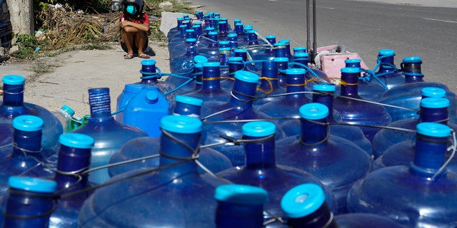 A boy sits beside water containers as residents line up for water as pipelines and electricity were damaged due to Typhoon Rai in Cebu province, central Philippines on Monday Dec. 20, 2021. 