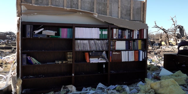 A bookcase left standing amidst rubble in Mayfield