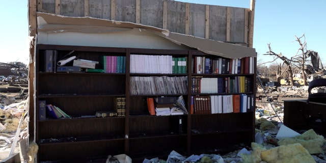 A bookcase left standing amidst rubble in Mayfield