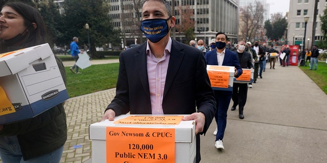 Solar energy advocates carry boxes of petitions against proposed reforms that they claim would handicap the rooftop solar market to the governor's office at the Capitol in Sacramento, California, Wednesday, Dec. 8, 2021. 