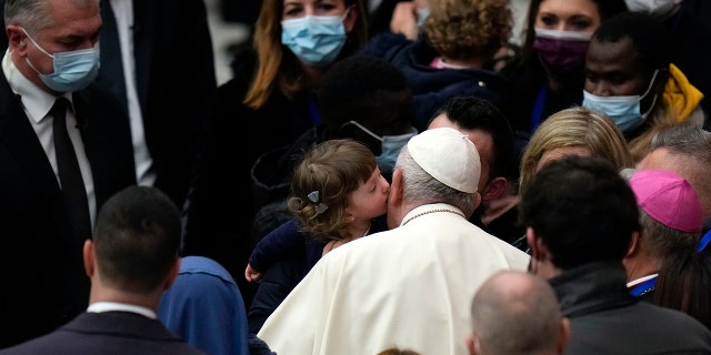 Pope Francis is kissed by a child at the end of his weekly general audience in the Paul VI Hall, at the Vatican, Wednesday, Dec. 22, 2021.