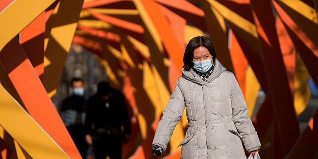 A woman wearing a face mask to help protect from the coronavirus looks as she walks by an art installation depicting a prosperity chamber on display outside a mall in Beijing, Monday, Dec. 27, 2021. 