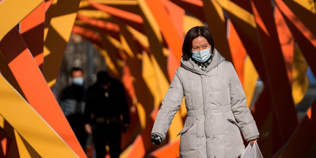 A woman wearing a face mask to help protect from the coronavirus looks as she walks by an art installation depicting a prosperity chamber on display outside a mall in Beijing, Monday, Dec. 27, 2021. 