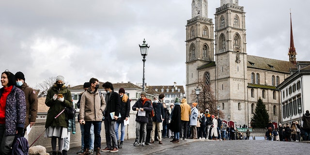 People queue from the Muenster Bridge to the Zurich City Hall to cast their ballot at the City Hall polling station to vote in a COVID-19 referendum, in Zurich, Switzerland, Sunday, Nov. 28, 2021. The coronavirus's omicron variant kept a jittery world off-kilter Wednesday Dec. 1, 2021, as reports of infections linked to the mutant strain cropped up in more parts of the globe, and one official said that the wait for more information on its dangers felt like "an eternity."  
