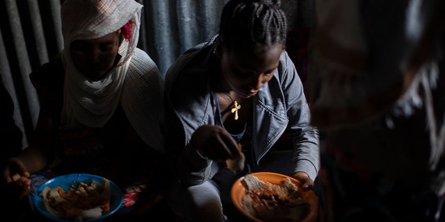 Displaced Tigrayan women, one wearing an Ethiopian Orthodox Christian cross, sit in a metal shack to eat food donated by local residents at a reception center for the internally displaced in Mekele, in the Tigray region of northern Ethiopia, on May 9, 2021. 