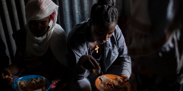 Displaced Tigrayan women, one wearing an Ethiopian Orthodox Christian cross, sit in a metal shack to eat food donated by local residents at a reception center for the internally displaced in Mekele, in the Tigray region of northern Ethiopia, on May 9, 2021.