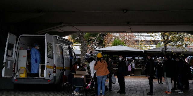 A member of the medical staff at the National Public Health Organisation (EODY) conducts a COVID-19 rapid test on a woman as others wait in a queue in Athens, Greece, Wednesday, Dec. 29, 2021.