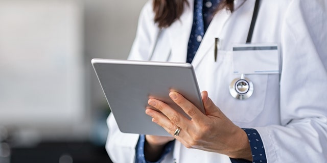 Close up of woman doctor hands using digital tablet at clinic. Closeup of female doctor in labcoat and stethoscope holding digital tablet, reading patient report. 