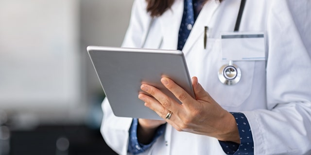 Close up of woman doctor hands using digital tablet at clinic. Closeup of female doctor in labcoat and stethoscope holding digital tablet, reading patient report. 