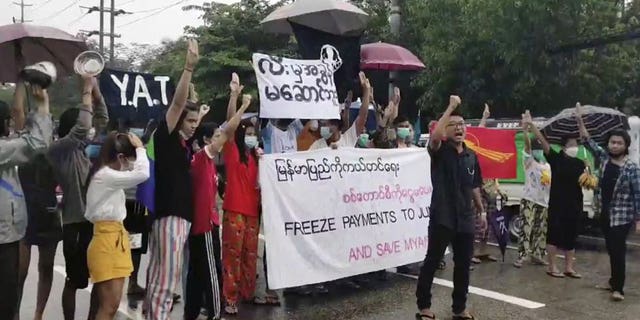 Protesters hold signs in Yangon on Oct. 30, 2021, calling for the freezing of revenues from oil and gas sales in Myanmar.