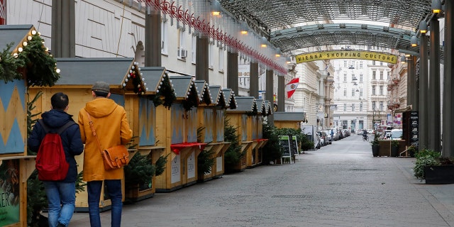 Two people walk by closed Christmas markets and shops due to the lockdown in Vienna, Austria, Tuesday, Nov. 30, 2021.