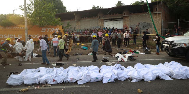 Bodies in bodybags are placed on the side of the road after an accident in Tuxtla Gutierrez, Chiapas state, Mexico, Dec. 9, 2021. Mexican authorities say at least 49 people were killed and dozens more injured when a cargo truck carrying Central American migrants rolled over on a highway in southern Mexico.