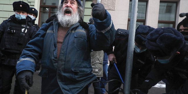 Police officers unlock a man who chained himself to a pole in front of the Supreme Court of the Russian Federation in Moscow, Russia, Tuesday, Dec. 28, 2021.
