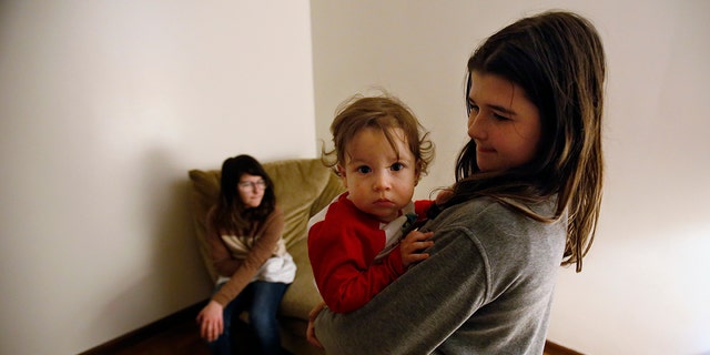 Abby Olmstead, age 10, holds her 1-year-old brother, Liam Myers, while her 13-year-old sister Makayla Olmstead sits on the couch, on Thursday, Dec. 2, 2021, at their home in Paw Paw, Michigan. Abby has been working with support staff at her school to manage her emotions in the classroom at Paw Paw Elementary School. She said she sometimes feels anxious and blurts out things in class. Mindfulness exercises help calm and distract her, she said. She said the behavior specialist at her school "always makes me laugh when I have anxiety, and that's not a bad thing." 