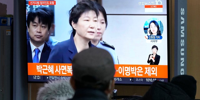 People watch a TV screen showing a file image of former South Korean President Park Geun-hye during a news program at the Seoul Railway Station in Seoul, South Korea, Friday, Dec. 24, 2021. The South Korean government said Friday it will grant a special pardon to Park, who is serving a lengthy prison term for bribery and other crimes. The Korean letters read "Pardon Park Geun-he."