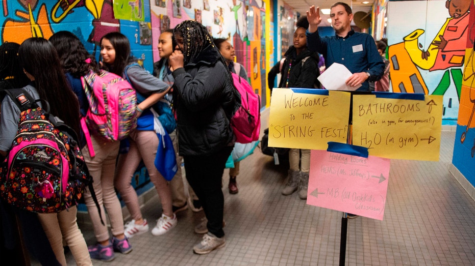 A teacher directs students to their rooms to get their instruments for the Baltimore Symphony Orchestra's OrchKids program during the String Fling concert at the Lockerman Bundy Elementary School in Baltimore, Maryland, on March 12, 2019. - As the conductor raises her baton, dozens of children come to order, and their everyday cacophonous chatting gives way to a melodic cascade of notes. The 60 or so students are part of OrchKids, a program run by the Baltimore Symphony Orchestra, which is hoping to bring change to the troubled city through the power of music. (Photo by Jim WATSON / AFP) (Photo credit should read JIM WATSON/AFP via Getty Images)