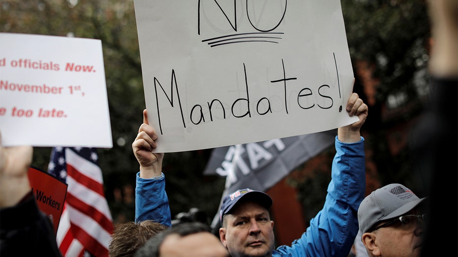 Mask mandate protester holds sign reading "No Mandates!"