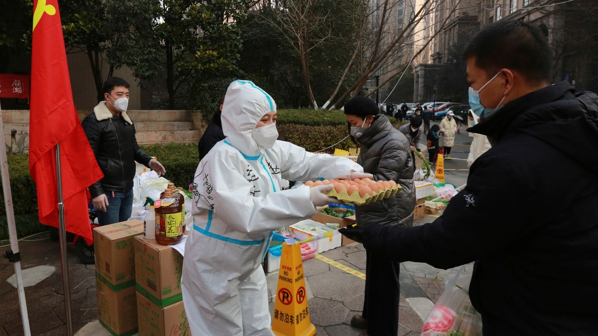 A community volunteer hands over eggs to a buyer at a temporary food store to provide supplies to residents outside a residential block in Xi'an city in northwest China's Shaanxi province Monday, Jan. 03, 2022. (Chinatopix Via AP)