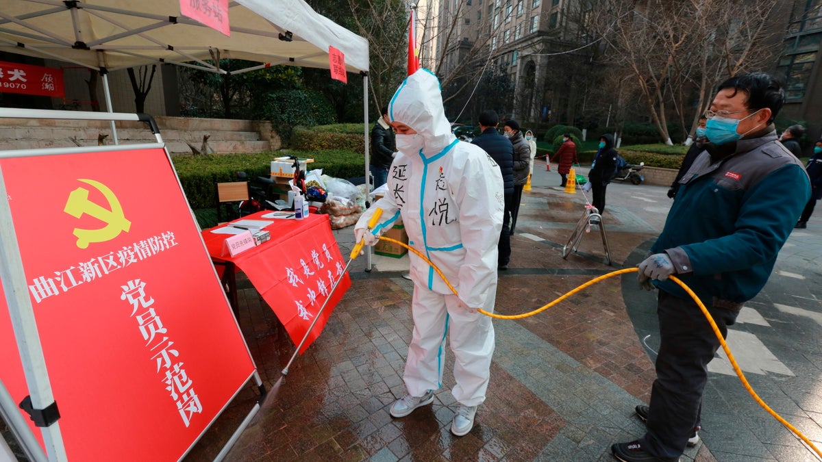 Government workers disinfect a work post with the sign "Model Community Party Post" outside a residential block in Xi'an city in northwest China's Shaanxi province Monday, Jan. 3, 2022. Authorities in the northern Chinese city of Xi'an say they can provide food, health care and other necessities for the roughly 13 million under an almost two-week old lockdown. But some residents describe difficulties obtaining supplies and frustration and the economic impact on the city that is home to the famed Terracotta warriors, along with major industries. (Chinatopix Via AP)
