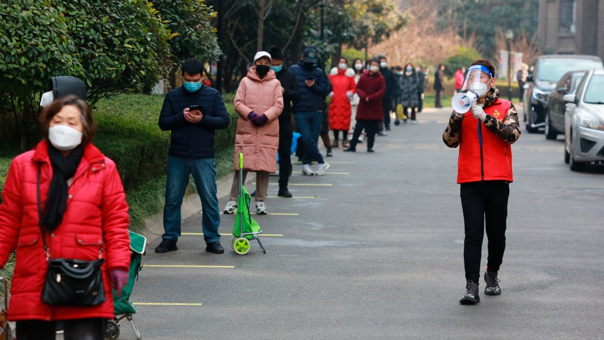 A community volunteer uses a megaphone to remind residents to keep their social distance as they line up to collect their daily necessities outside a residential block in Xi'an city in northwest China's Shaanxi province Monday, Jan. 3, 2022. (Chinatopix Via AP)