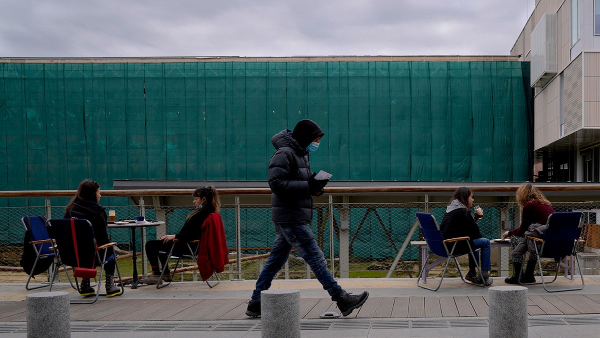 A man wearing a face mask to protect from coronavirus, walks past customers of a coffee shop in central Nicosia, Cyprus, Wednesday, Jan. 5, 2022.