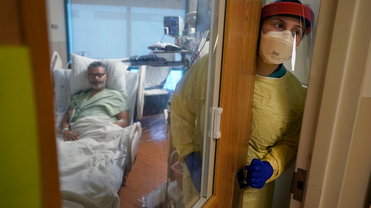 Registered nurse Rachel Chamberlin, of Cornish, N.H., right, steps out of an isolation room where where Fred Rutherford, of Claremont, N.H., left, recovers from COVID-19 at Dartmouth-Hitchcock Medical Center, in Lebanon, N.H. (AP Photo/Steven Senne)