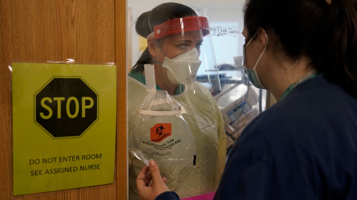 Clinical Nurse Supervisor Melinda Chapin, of Holderness, N.H., left, communicates through glass from inside a COVID-19 isolation room with registered nurse Rachel Chamberlin, of Cornish, N.H., right, at Dartmouth-Hitchcock Medical Center, in Lebanon, N.H. (AP Photo/Steven Senne)
