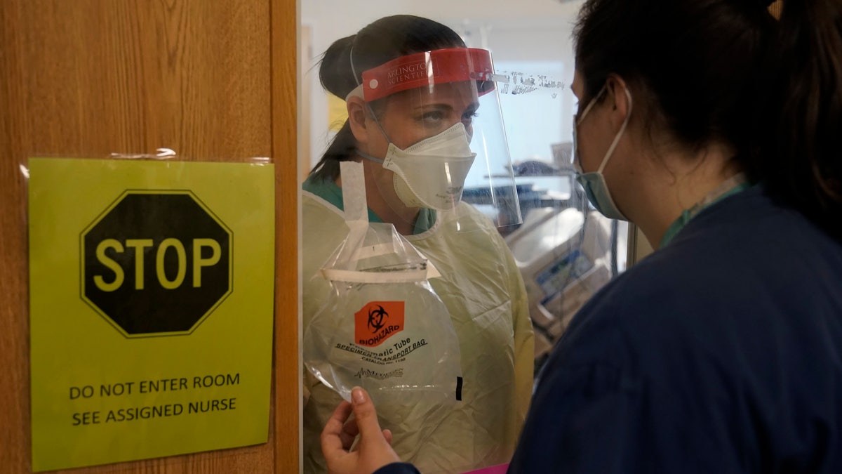 Clinical Nurse Supervisor Melinda Chapin, of Holderness, N.H., left, communicates through glass from inside a COVID-19 isolation room with registered nurse Rachel Chamberlin, of Cornish, N.H., right, at Dartmouth-Hitchcock Medical Center, in Lebanon, N.H. (AP Photo/Steven Senne)