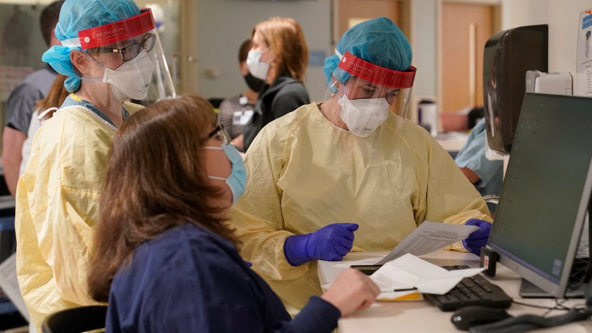 Registered nurses Sarah Carr, top left, and Lindsay Holloran, right, are suited up with protective gear before entering a patient's room at the COVID-19 Intensive Care Unit at Dartmouth-Hitchcock Medical Center, in Lebanon, N.H.(AP Photo/Steven Senne)