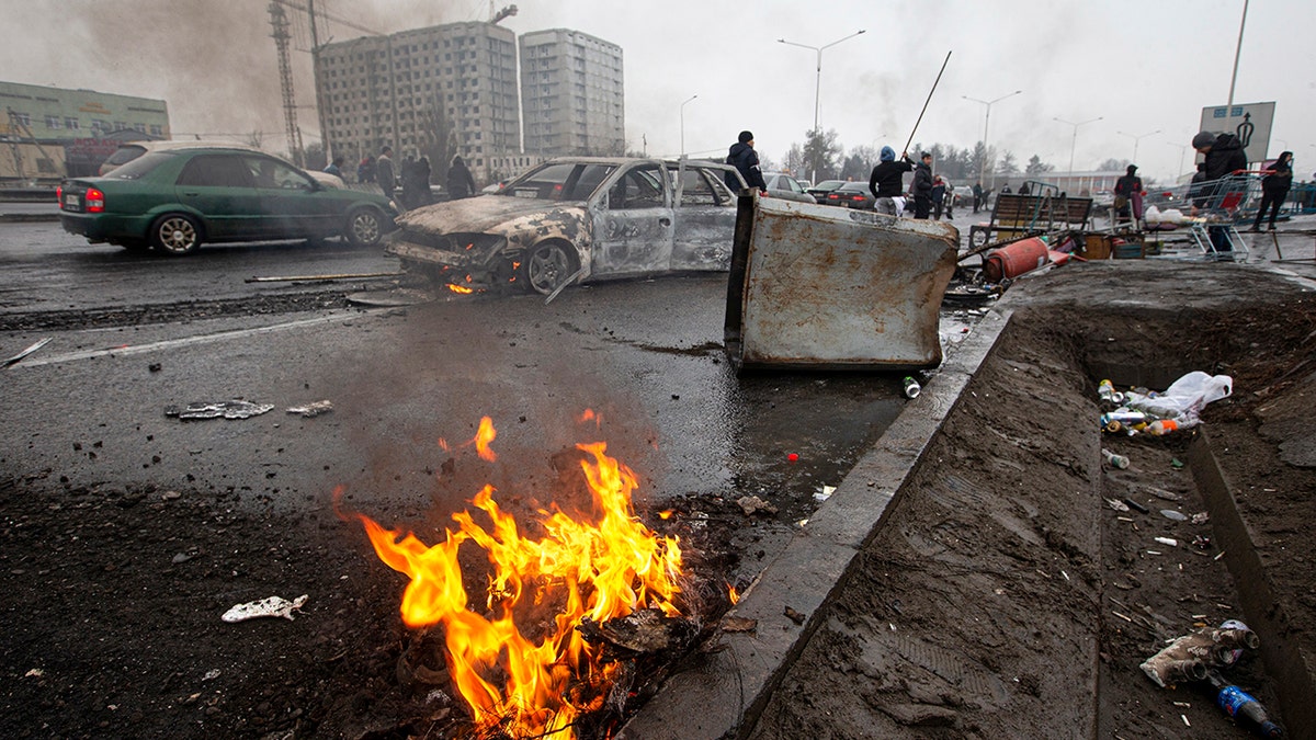 People walk past cars, which were burned after clashes, on a street in Almaty, Kazakhstan, Friday, Jan. 7, 2022.