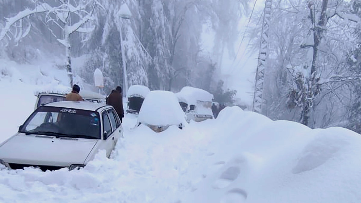 People walk past vehicles trapped in a heavy snowfall-hit area in Murree, some 28 miles (45 kilometers) north of the capital of Islamabad, Pakistan, Saturday, Jan. 8, 2022. (Inter Services Public Relations via AP)