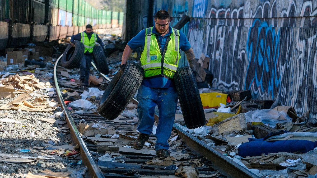 Contractor workers Adam Rodriguez, front, and Luis Rosas pick up vehicle tires from the shredded boxes and packages at a section of the Union Pacific train tracks in downtown Los Angeles Friday, Jan. 14, 2022. (AP Photo/Ringo H.W. Chiu)