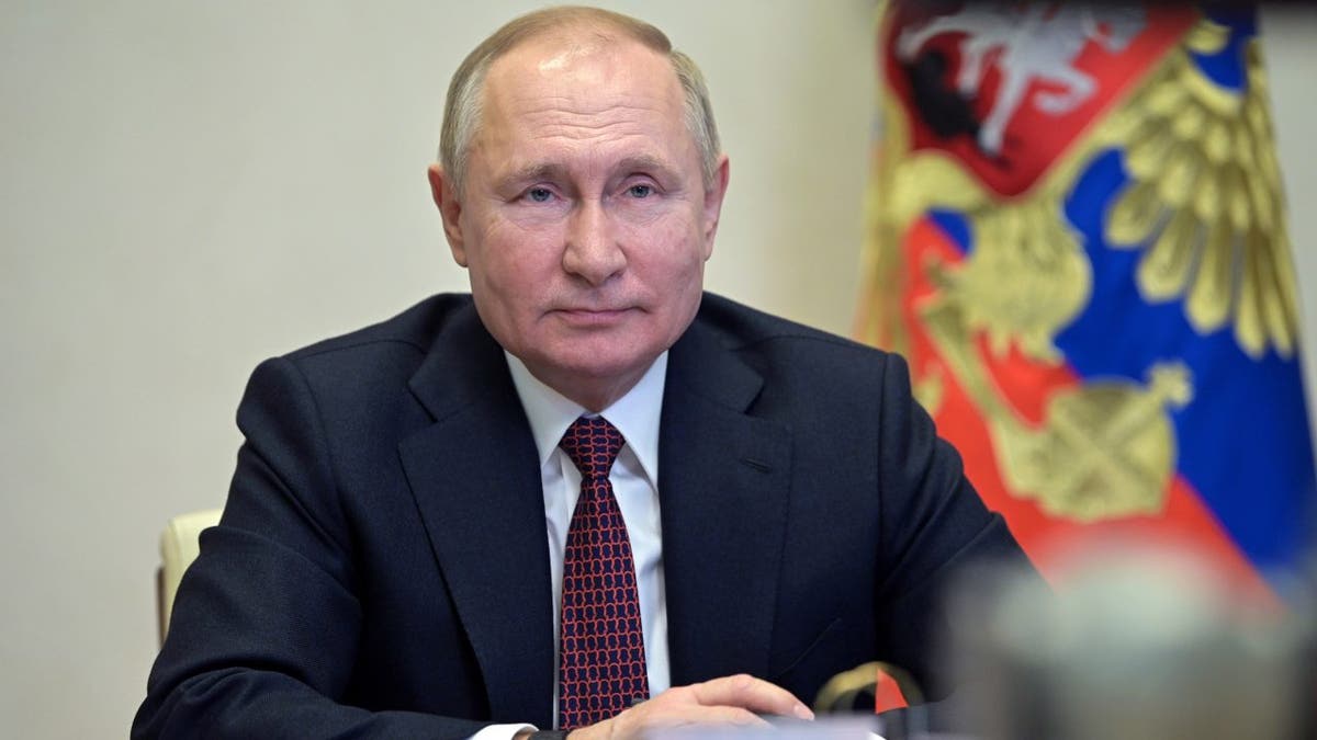 Russian President Vladimir Putin sitting at table wearing black suit and red tie