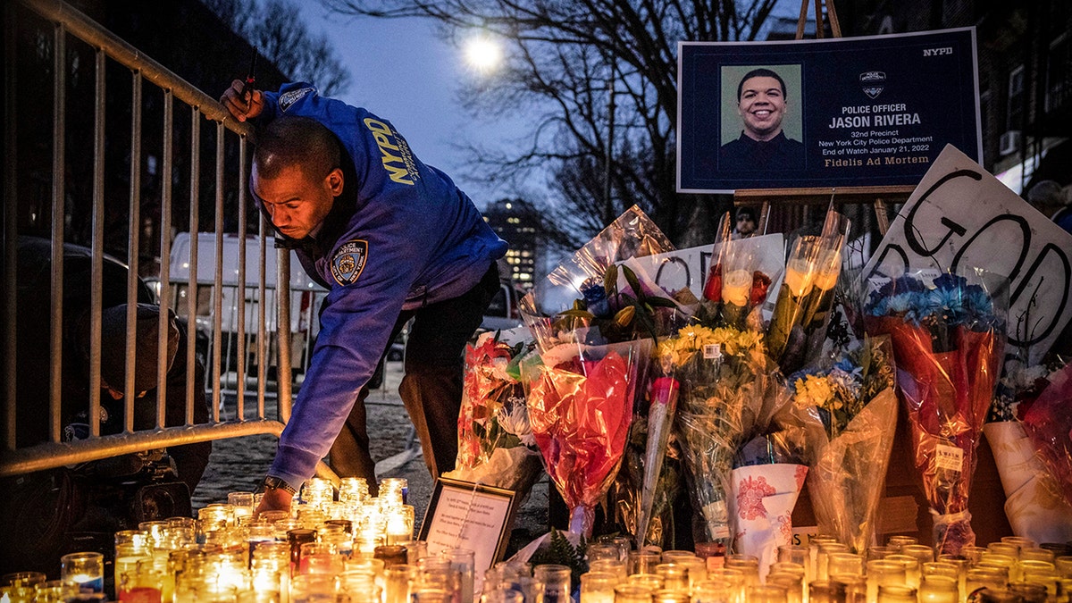New York City Police Department officer lights a candle at a makeshift memorial outside the NYPD's 32nd Precinct