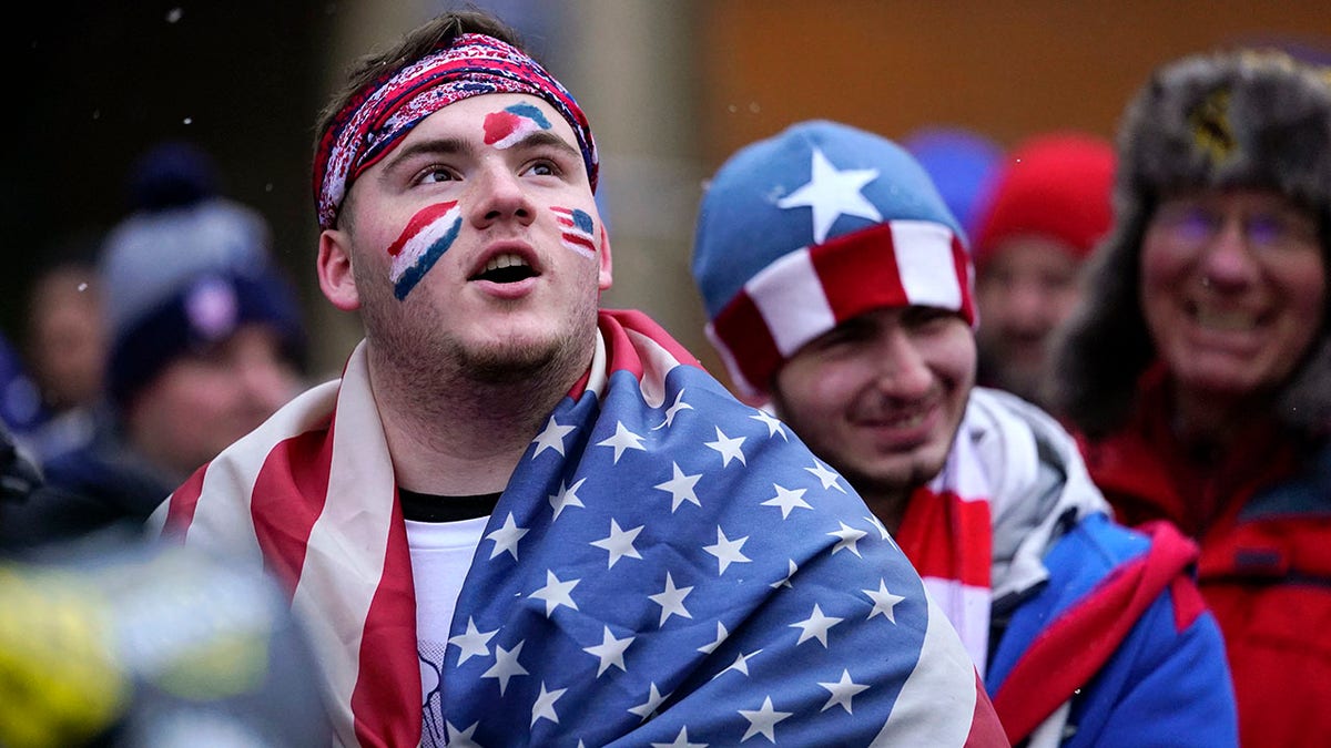 A man is draped in the United States flag as a group of U.S. men's national soccer team supporters march to Lower.com Field ahead of a FIFA World Cup qualifying soccer match against El Salvador, Thursday, Jan. 27, 2022, in Columbus, Ohio.