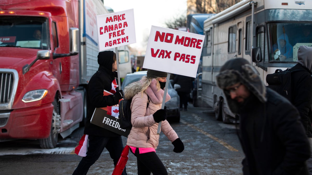 People walk in front of trucks parked on Wellington Street as they join a rally against COVID-19 restrictions on Parliament Hill, which began as a cross-country convoy protesting a federal vaccine mandate for truckers, in Ottawa, on Saturday, Jan. 29, 2022. (Justin Tang/The Canadian Press via AP)