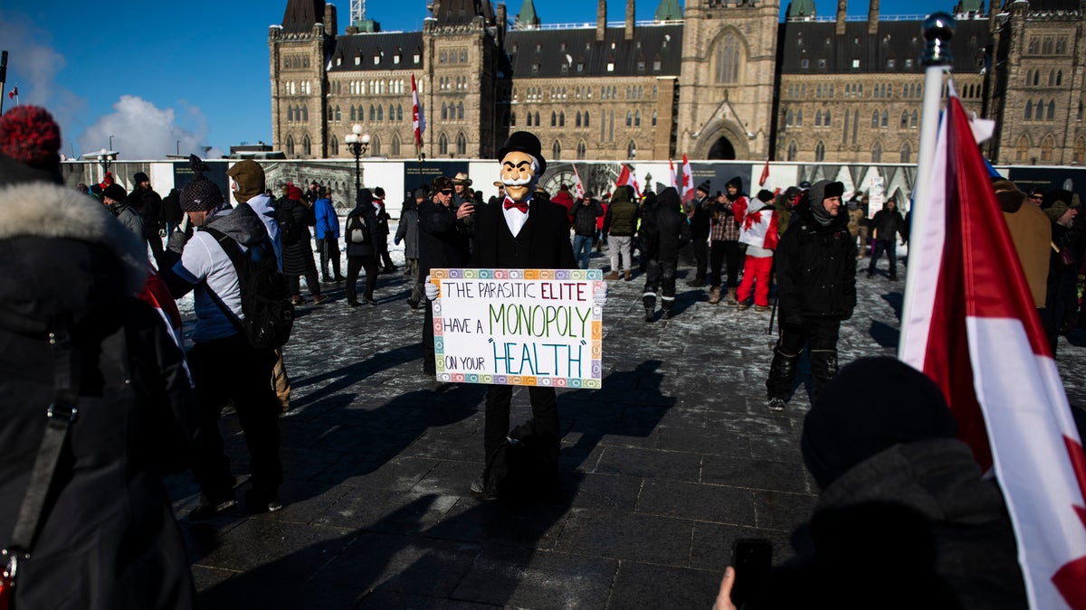 A person wearing a Monopoly Man mask holds a sign during a rally against COVID-19 restrictions on Parliament Hill, which began as a cross-country convoy protesting a federal vaccine mandate for truckers, in Ottawa, on Saturday, Jan. 29, 2022.