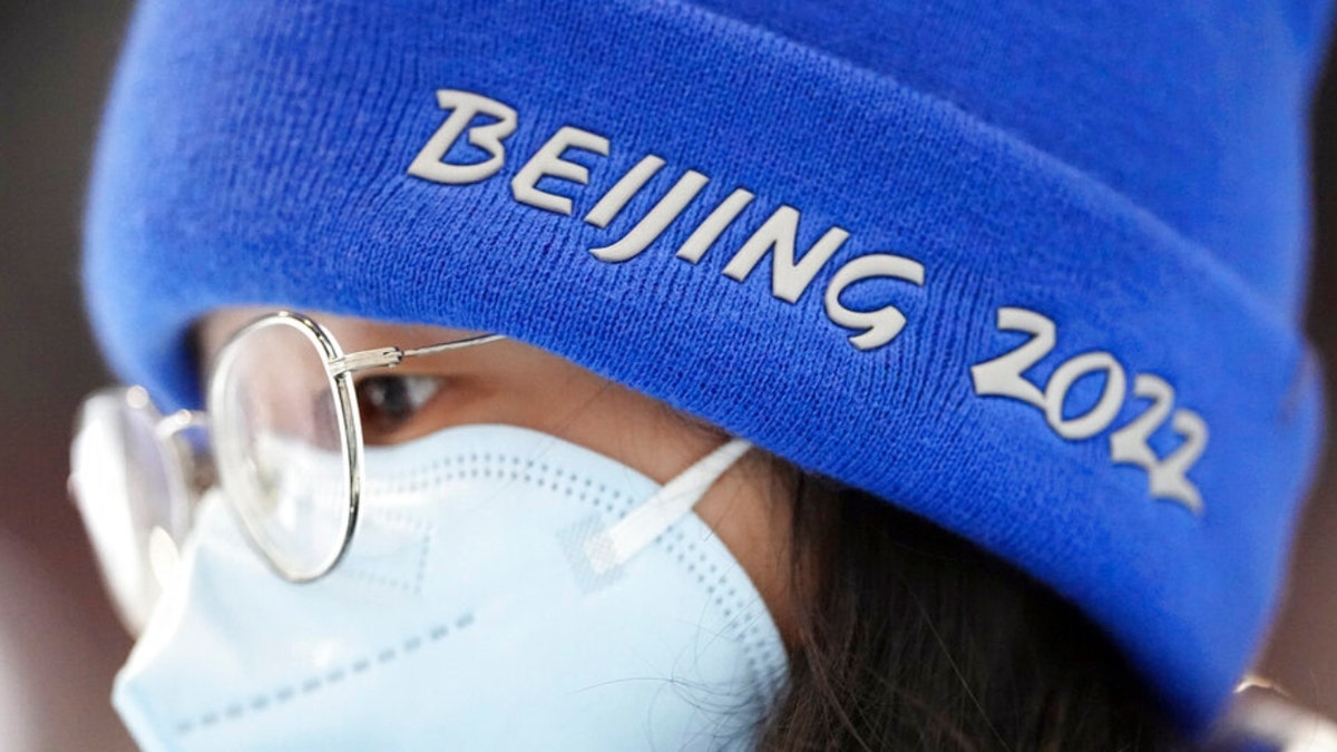 A woman wears a Beijing 2022 hat while walking inside the main media center at the 2022 Winter Olympics, Saturday, Jan. 22, 2022, in Beijing.