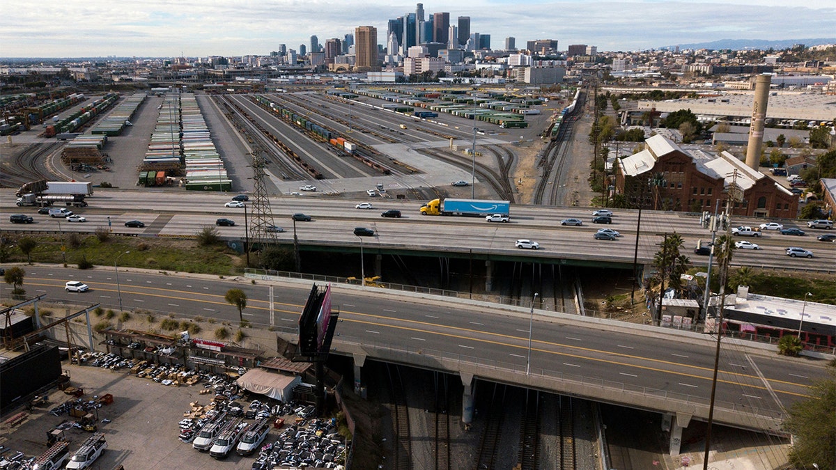 An aerial image from Jan. 16, 2022 shows the Los Angeles skyline as a semi-truck carrying an Amazon Prime trailer crosses a bridge over a section of Union Pacific train tracks.