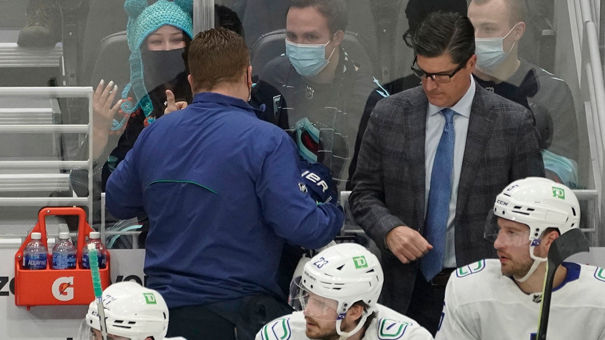 Seattle Kraken fan Nadia Popovici, upper left, gestures toward Vancouver Canucks assistant equipment manager Brian "Red" Hamilton, second from left, after they were introduced during the first period of an NHL hockey game, Saturday, Jan. 1, 2022, in Seattle.