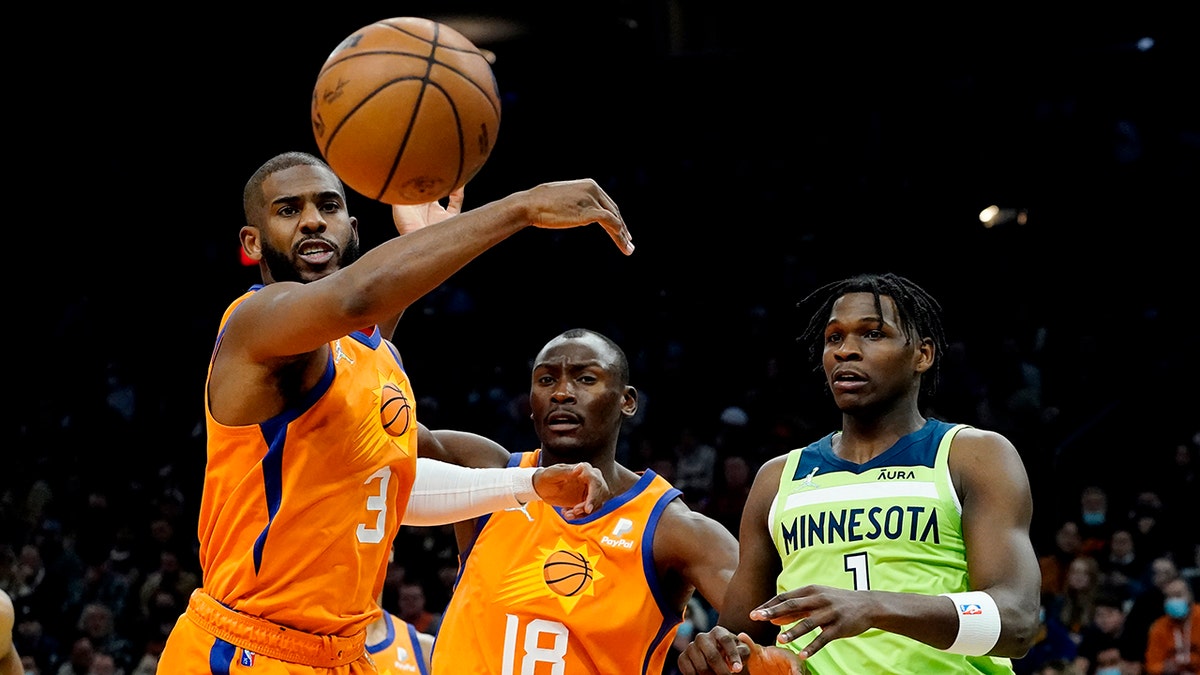 Phoenix Suns guard Chris Paul (3) reaches for a loose ball as Minnesota Timberwolves forward Anthony Edwards (1) and Phoenix Suns center Bismack Biyombo (18) look on during the first half of an NBA basketball game, Friday, Jan. 28, 2022, in Phoenix.