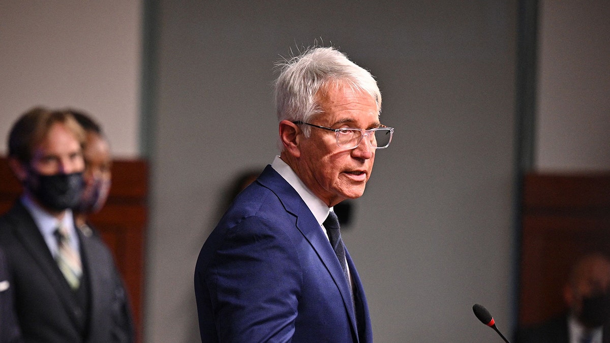 George Gascon speaks in front of a microphone in a navy suit at a news briefing